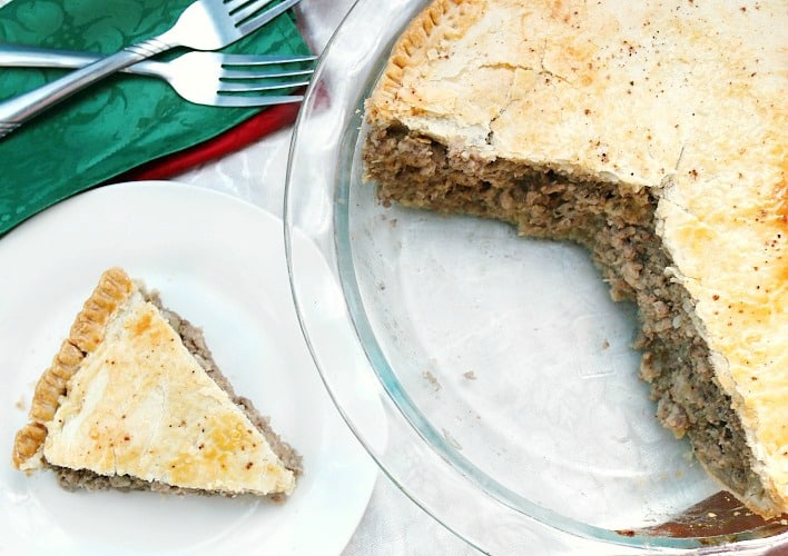 Slice of pork pie recipe or tourtiere recipe on white plate with fork