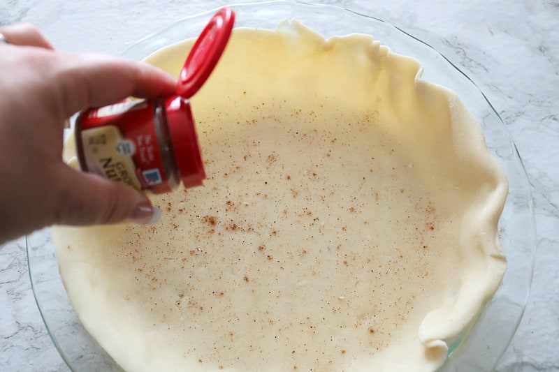 Sprinkling nutmeg onto pie crust for tourtiere recipe