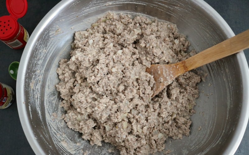 Mixing pork mixture for meat pie in large stainless steel bowl