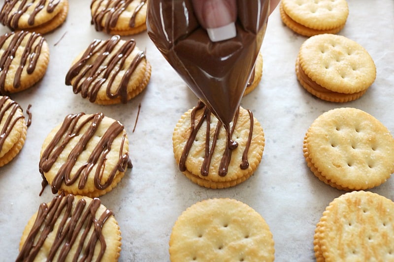 hand drizzling chocolate over crackers. 