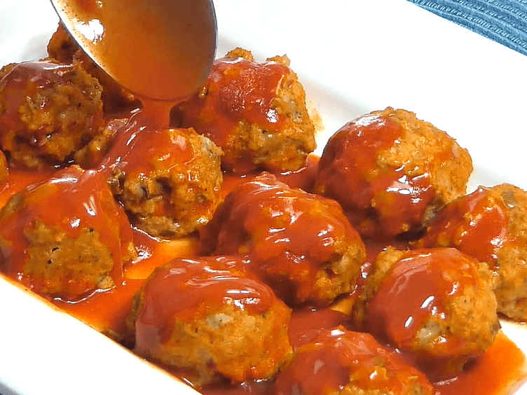 a spoon drizzling buffalo sauce over meatballs. 