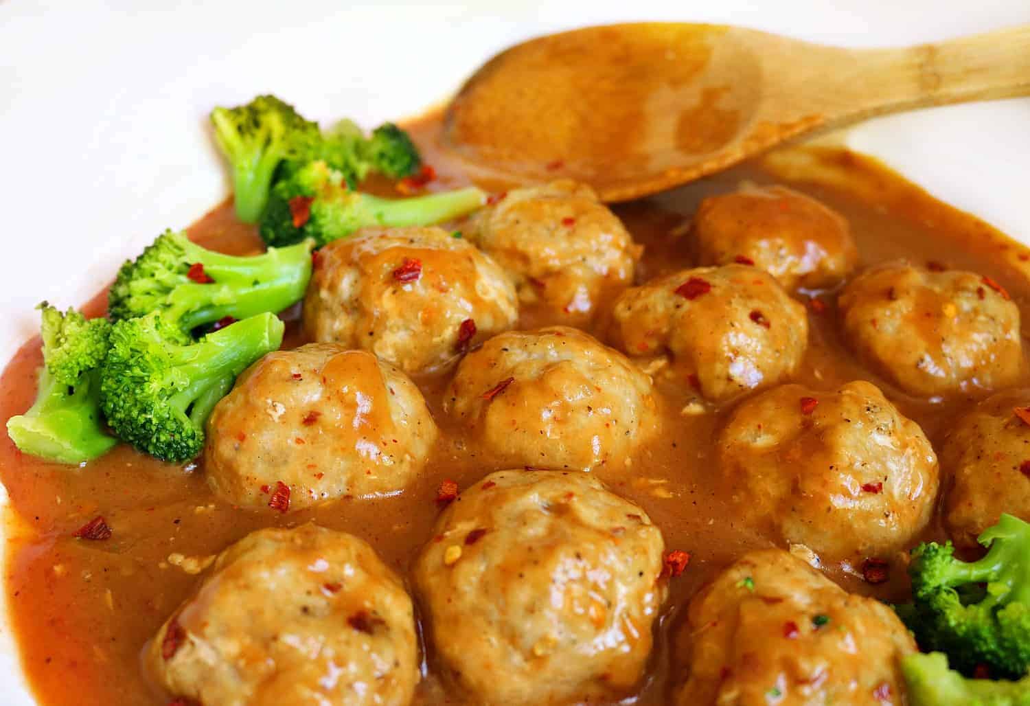 a bowl full of meatballs in sauce with wooden spon.