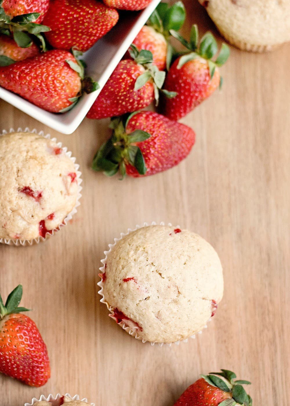 two low carb strawberry muffins on wood cutting board with berries.