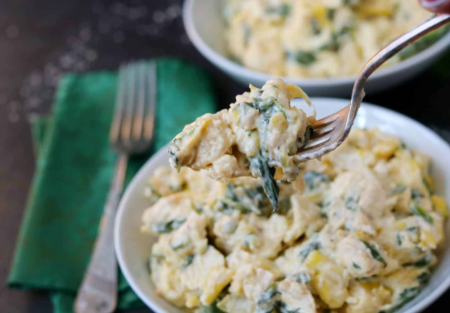 Instant Pot chicken with spinach, cheese, and artichokes held on a fork above bowl