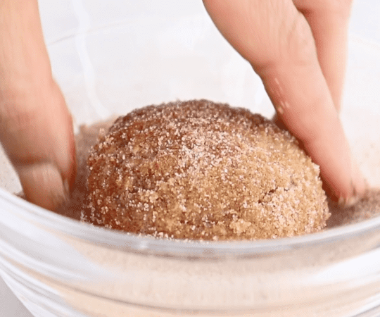 rolling a muffin in cinnamon sugar in a bowl. 