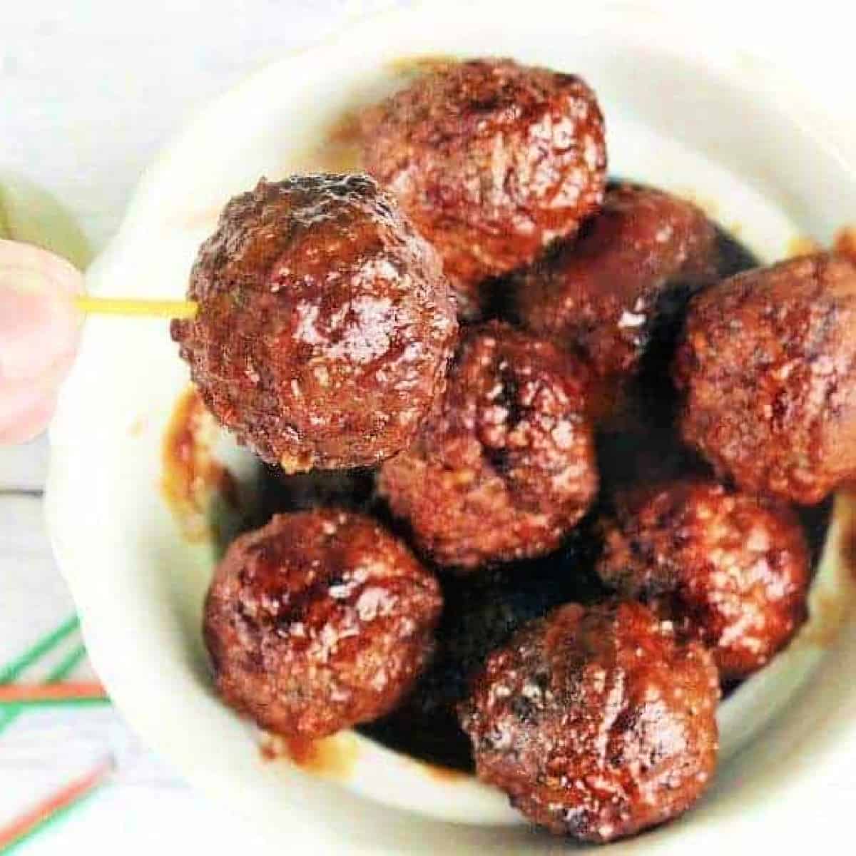 a bowl full of meatballs with one on a toothpick.