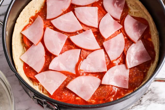 ham slices on pizza sauce. 