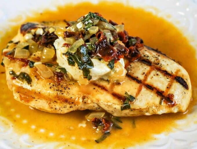 A piece of grilled chicken breast with lemon sauce on a plate. 