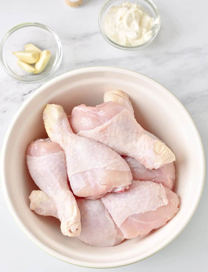 raw chicken drumsticks in bowl on counter. 