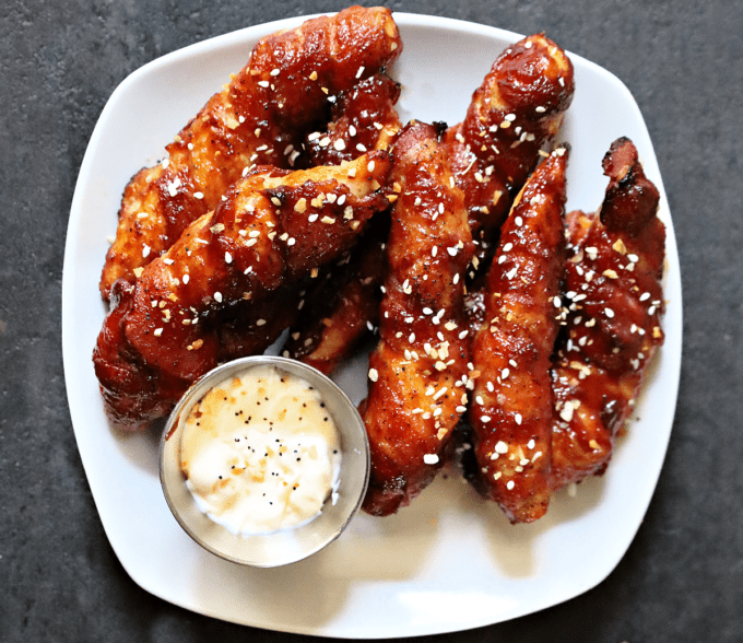 chicken tenders wrapped in bacon covered in bbq sauce on plate. 