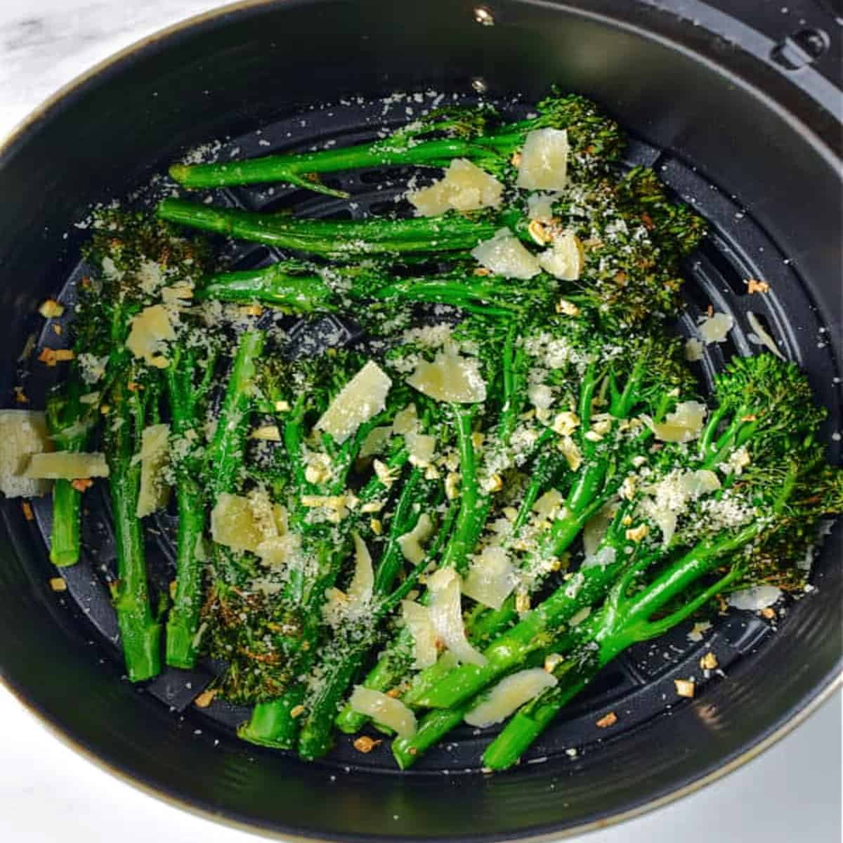 cooked broccolini in air fryer basket.