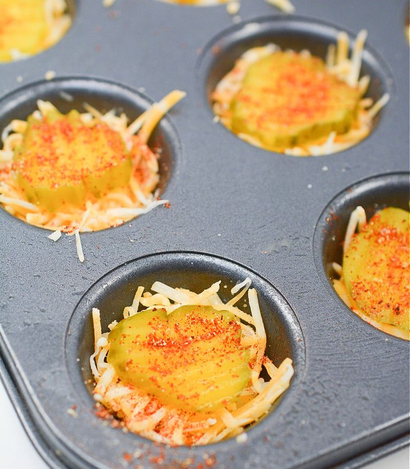 dill pickle slices on top of shredded cheese in muffin tin.