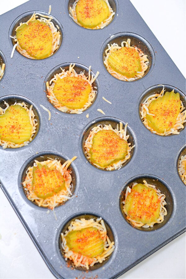 sliced pickle chips on shredded cheese in muffin pan. 