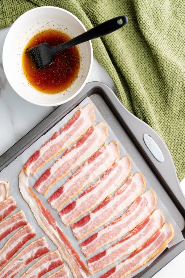 slices of raw bacon on sheet pan with dish of glaze. 