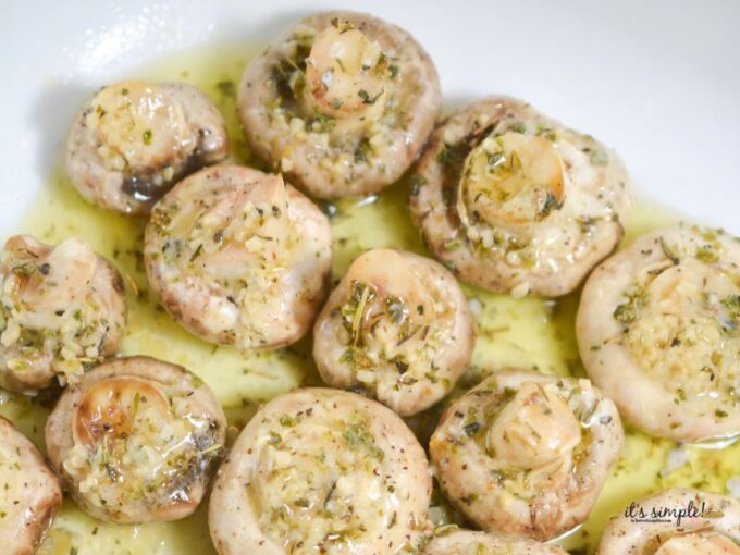 Garlic butter mixture being spooned over mushrooms in baking dish