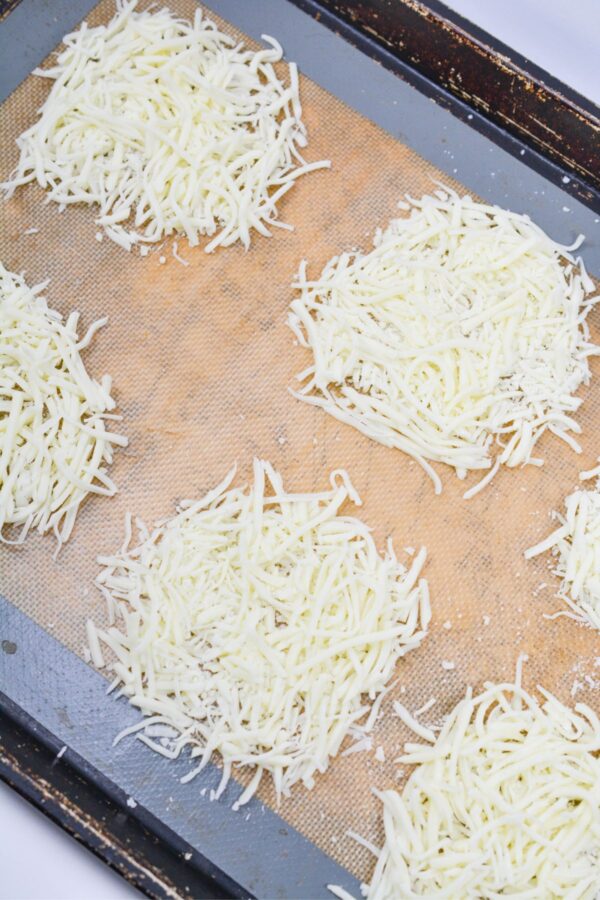 Sh​redde‌d mozza​rella cheese circles on a p‍archment-lin⁠ed b⁠akin‌g sheet.‍