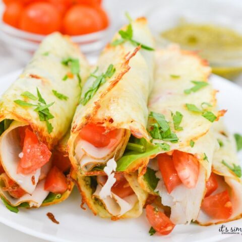 Keto Caprese Roll Ups made with crispy baked mozzarella, pesto, turkey, spinach, and tomatoes on a serving plate.