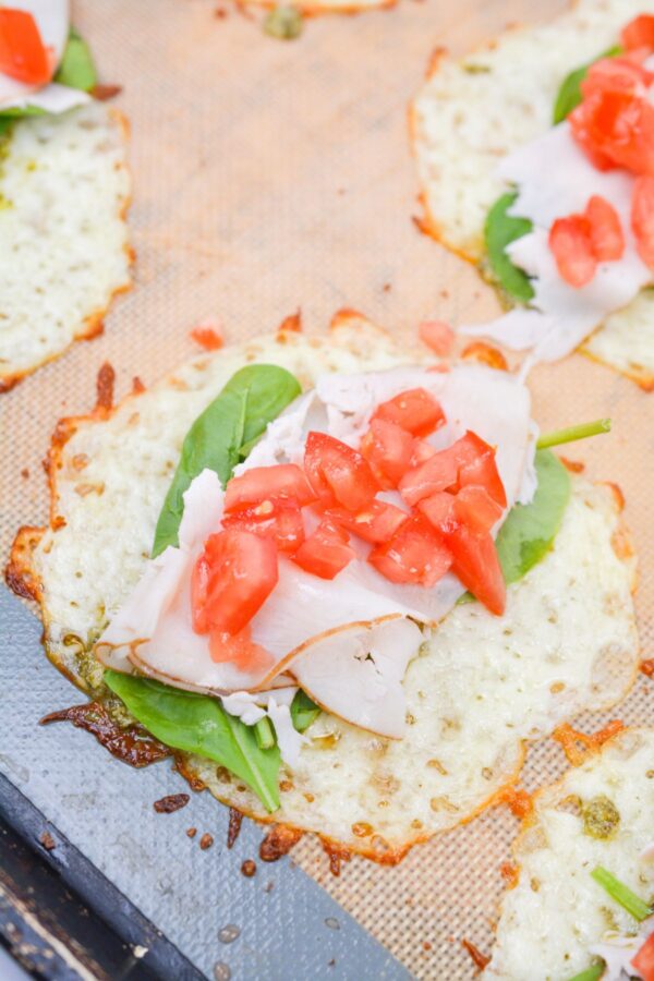 Pesto, spinach, turk‍ey,​ and chopped tomatoes layered ont​o baked mozzarella c⁠ircles before r‌ollin‍g.​
